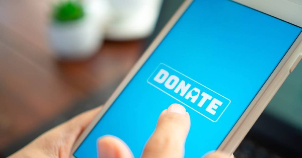 A close-up view of someone's finger tapping a blue screen with a white donation button on their cell phone.