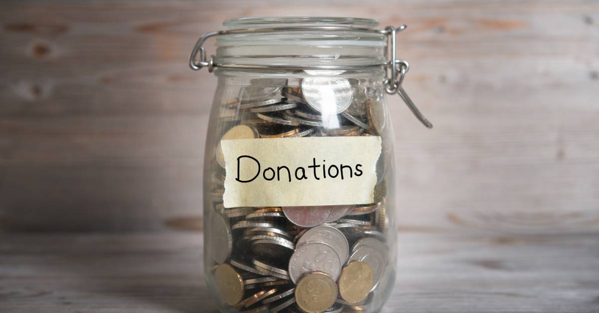 A small glass jar filled with different types of coins. The jar has a label on the outside that says "Donations."