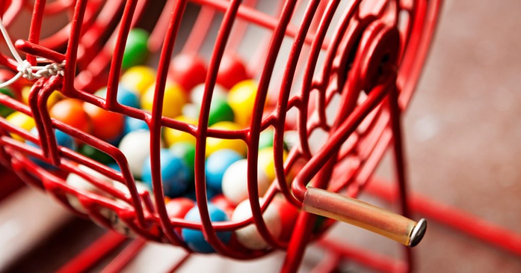 A close-up of a red lottery drawing machine with a variety of different colored balls inside the cage.