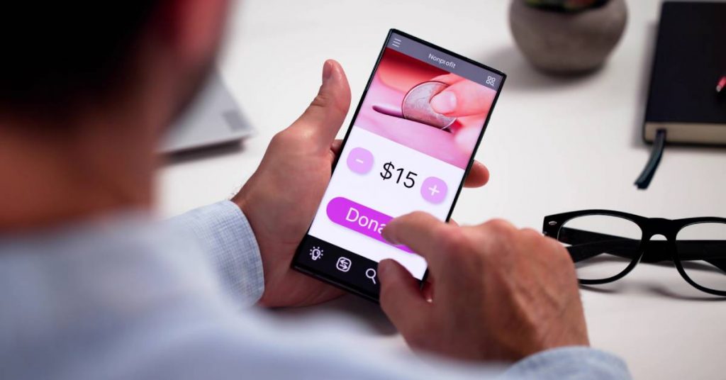 A man is using his smartphone and looking at an online donation screen. He is pressing a purple button that says "donate."