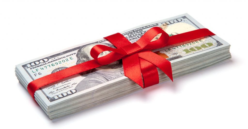 A stack of United States paper currency tied with a red fabric bow. The top of the stack has a $100 bill.