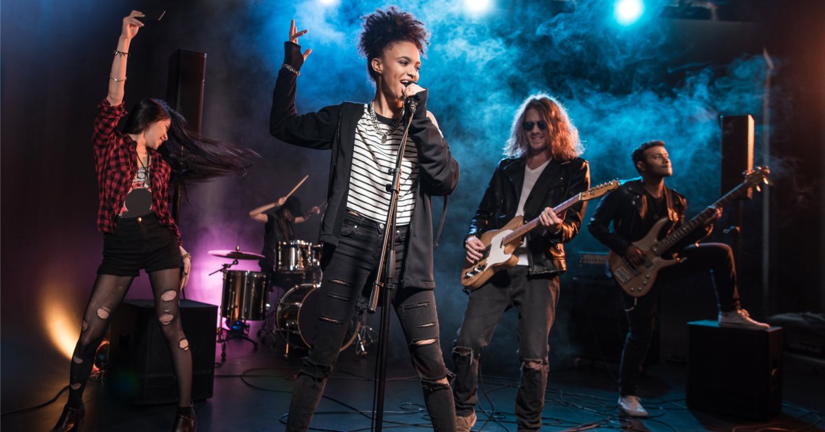 A band performing on stage. A female singer is holding a microphone while two men play guitar behind her.