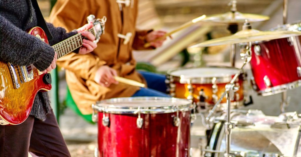 A close-up of two people playing music. One person is playing the guitar and the other person is playing the drums.