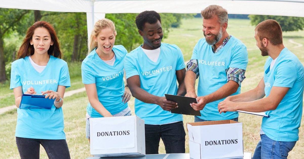 A group of adults in blue shirts with the word "volunteer" on them standing behind a table with two donation boxes.