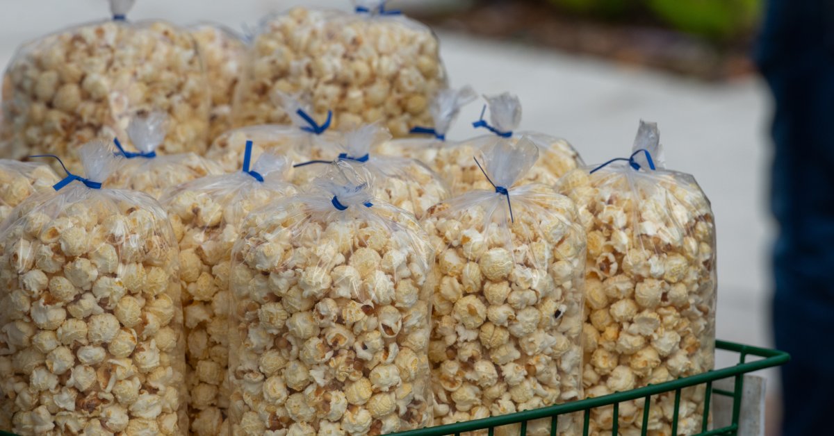 Multiple clear plastic bags of popcorn are tied with blue twist ties and organized in a green wire basket.